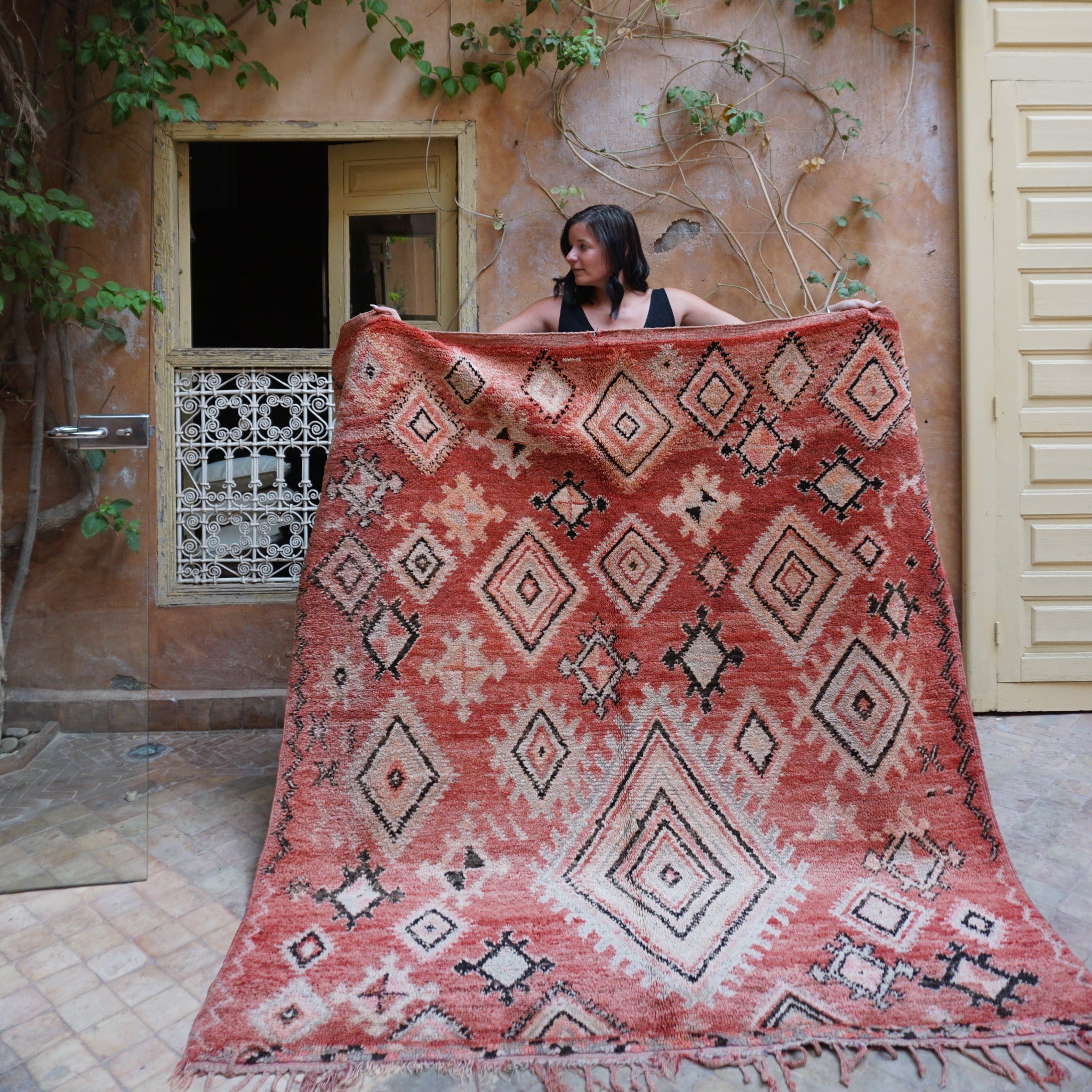 woman holding a large vintage red moroccan rug