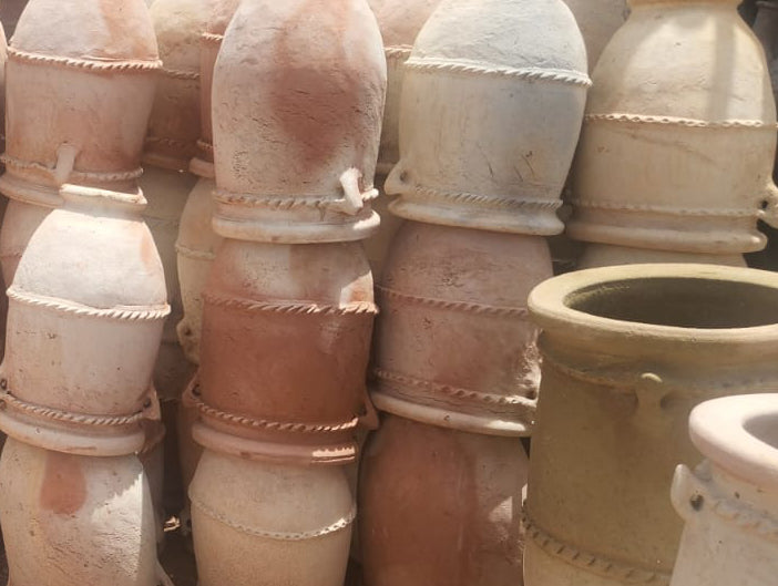 Stacks of terracotta pots in various sizes on a dirt floor with a brick wall background.